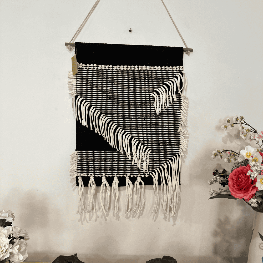 Monochrome cotton fringe wall hanging shown with wood rod detail